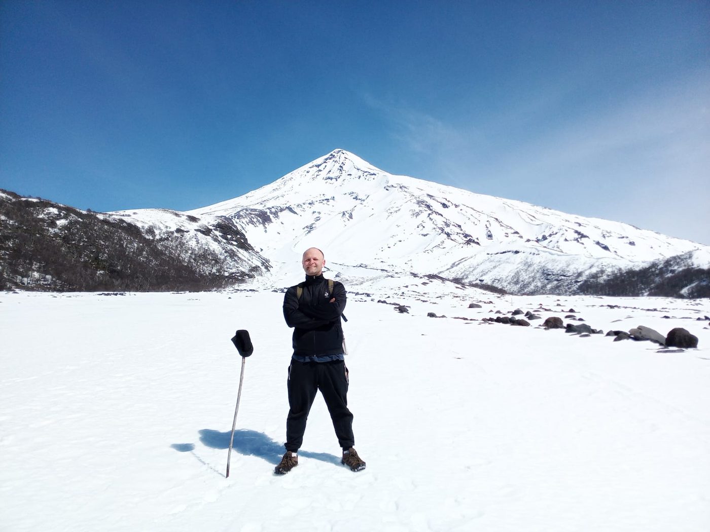 Pablo Barboni de pie en la nieve, con el volcán Lanín nevado y un cielo azul de fondo
